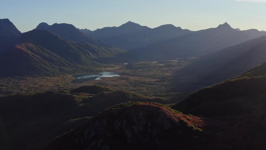 A slow aerial reveal of a stunning mountain valley at sunrise, with autumn colors on the hillsides and a tranquil lake in the distance