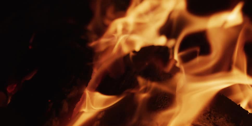 A close-up slow-motion view of warm, mesmerizing flames dancing over burning logs in the dark
