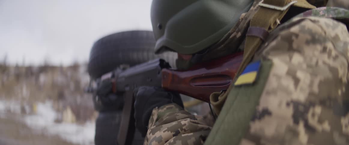A Ukrainian soldier in a helmet and camouflage uniform fires a rifle in slow motion during training in a snowy environment