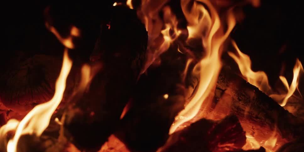 A close-up slow-motion shot of a cozy wood fire burning with bright orange flames in the dark