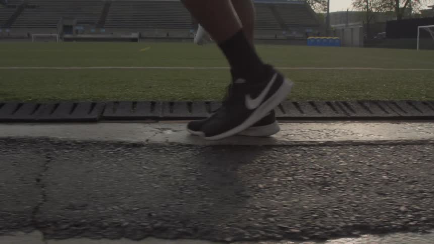 Person walks onto a field with bleachers in the background