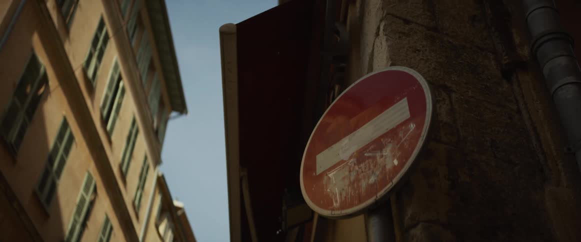 A close-up, low-angle shot captures a weathered red and white 'No Entry' sign on a historic European street