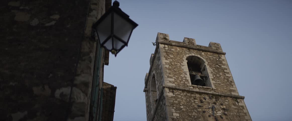 A slow focus pull reveals a historic stone bell tower with a vintage street lamp in the foreground