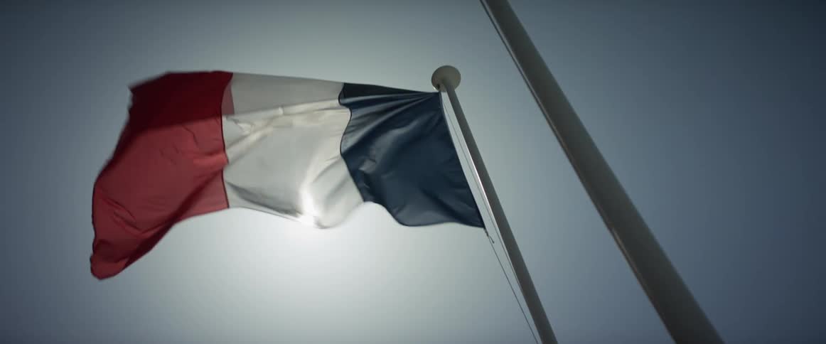 The French flag waves proudly in slow motion, backlit by the bright sun against a clear sky