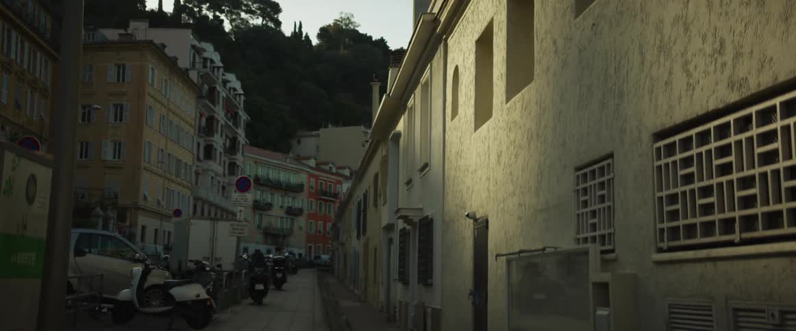 A slow camera tilt down reveals a quiet European street lined with buildings and parked scooters during golden hour