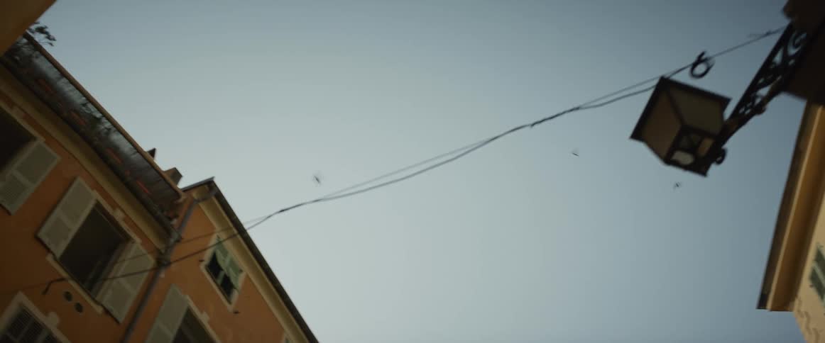 A slow, low-angle pan looks up at birds flying in the sky between old European buildings