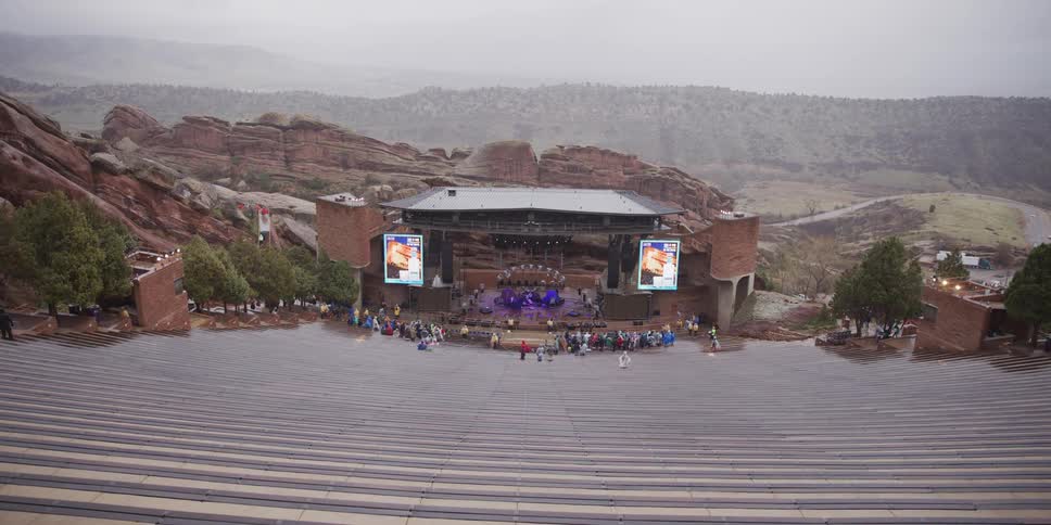 A band performs on stage for a small audience at the Red Rocks Amphitheatre on a rainy, overcast day