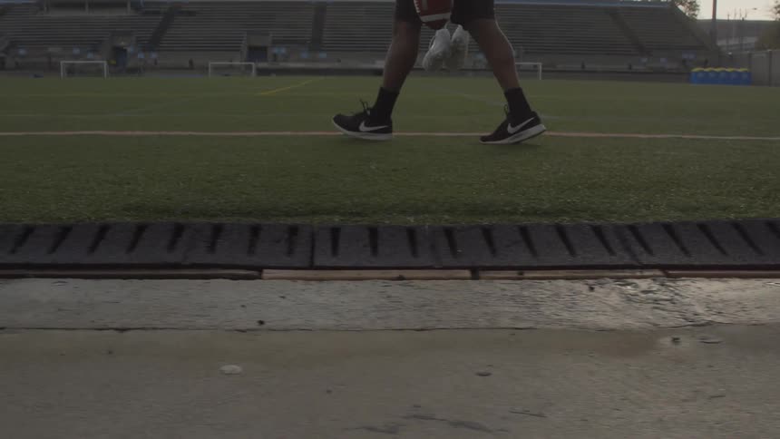 Person walks onto a field with bleachers in the background