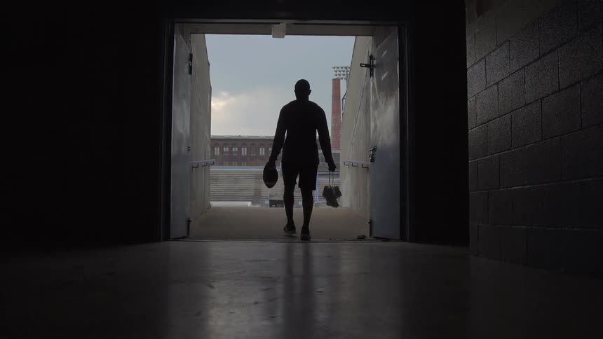 Person carrying bags walks down a hallway out to a stadium