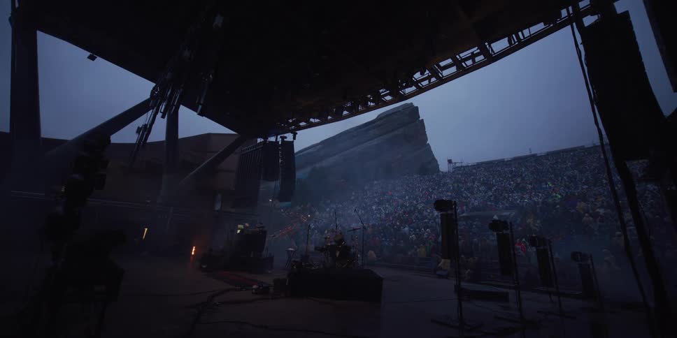 A wide view from backstage shows a massive crowd waiting for a concert to begin at the iconic Red Rocks Amphitheatre on a foggy evening