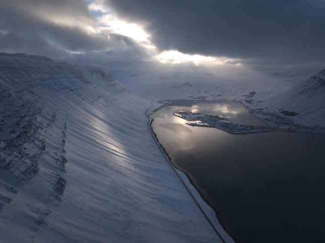 A majestic aerial view of a snow-covered Icelandic fjord and village as the sun breaks through dramatic clouds