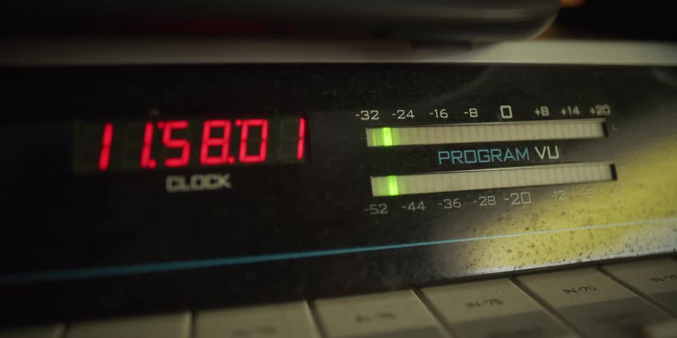 Vintage audio equipment features a ticking red digital clock and fluctuating green VU meters