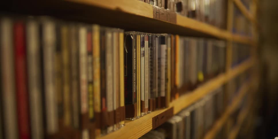 A slow pan across a wooden shelf packed with a large collection of music CDs