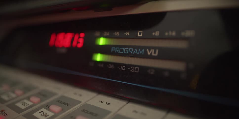 A close-up of a digital audio VU meter shows green LED bars fluctuating as they monitor sound levels in a studio