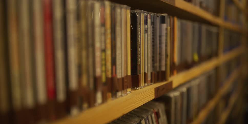 A slow pan across a wooden shelf filled with a large collection of music CDs in a vintage store