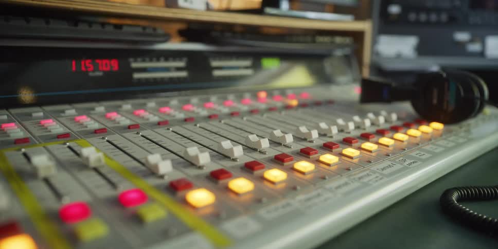 Dolly shot across a professional audio mixing console with illuminated buttons and sliders, ending on a pair of headphones