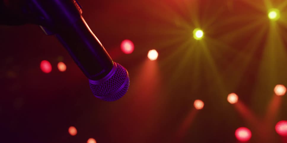 A microphone waits on a stand in front of colorful, glowing red and yellow stage lights before a live performance