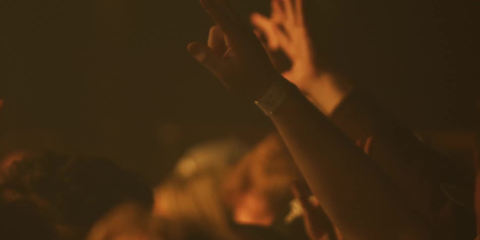 A crowd of people raise their hands in worship during a dimly lit concert or spiritual gathering