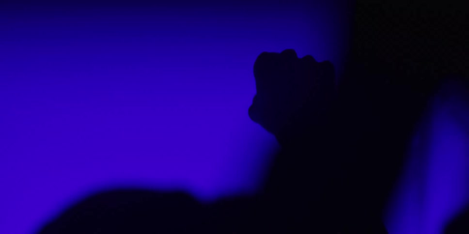 Silhouettes of a crowd of people dancing and raising their hands in the air at a concert with blue stage lights
