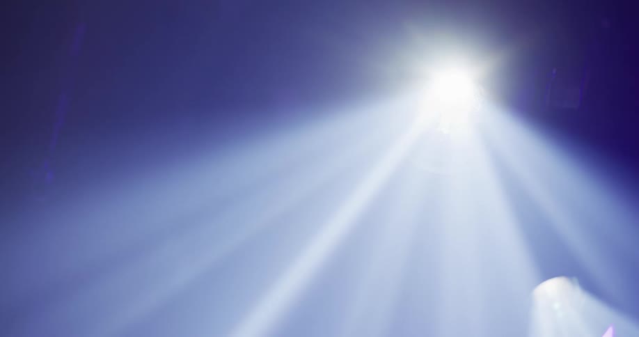A dramatic blue spotlight shines bright beams of light through a dark and hazy atmosphere