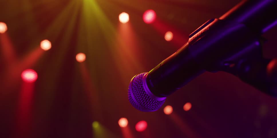 A microphone on stage is bathed in the warm, colorful glow of concert lighting