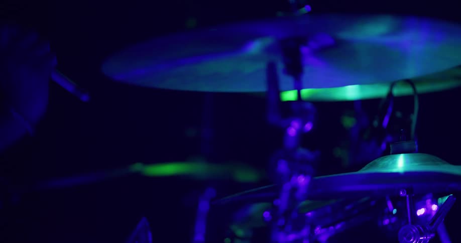 Close up of a drummer playing the cymbals in slow motion under dramatic green and blue lights during a performance