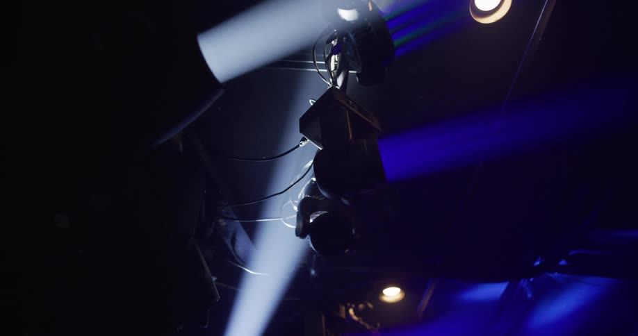 A slow pan across professional stage lights as blue and white beams cut through the hazy darkness of a venue