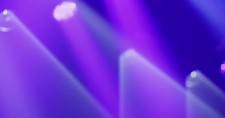 Soft, out-of-focus purple and blue stage lights shine through a hazy atmosphere, creating an abstract background
