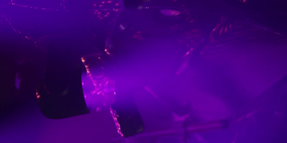 A colorful stage light projects beams of purple and yellow light through a smoky atmosphere