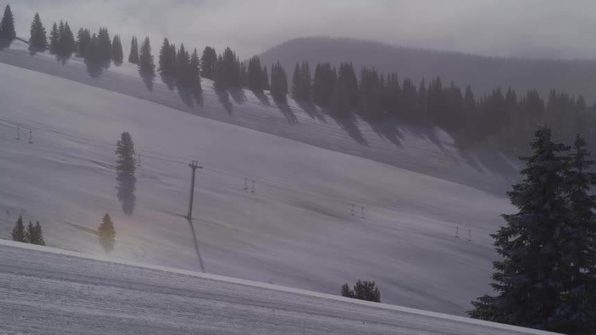 A serene, snowy mountain at a ski resort during a gentle snowstorm, with a faint sun dog visible in the misty air
