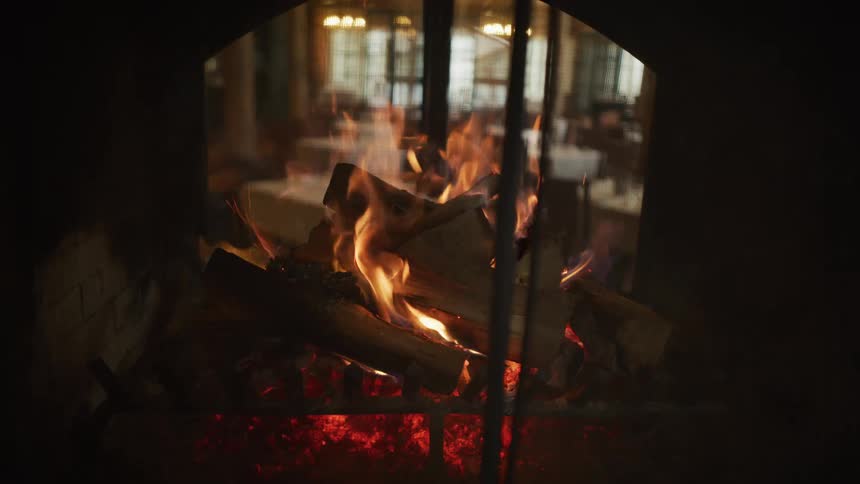 A slow-motion close-up shot captures the warmth of logs burning in a cozy restaurant fireplace