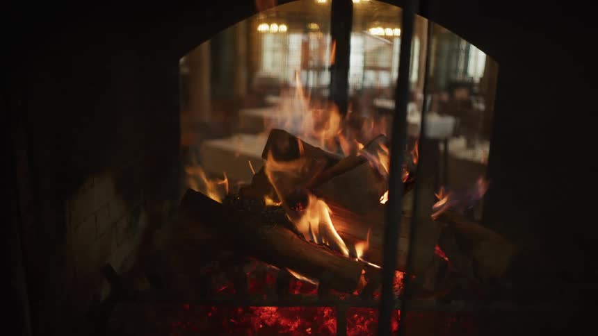 Logs burn brightly in a cozy fireplace, creating a warm and inviting atmosphere in a restaurant