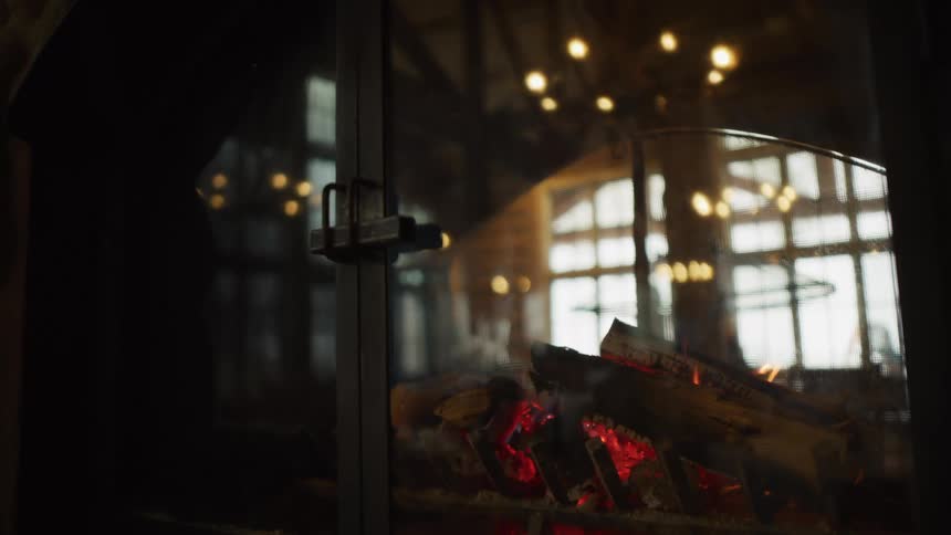 Burning logs in a glass-enclosed fireplace create a warm and cozy atmosphere in a rustic lodge