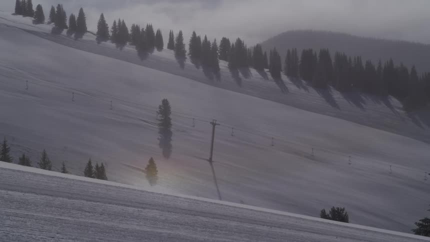 A snowy mountain ski slope with a sun dog and snowfall in a winter landscape with evergreens and a ski lift