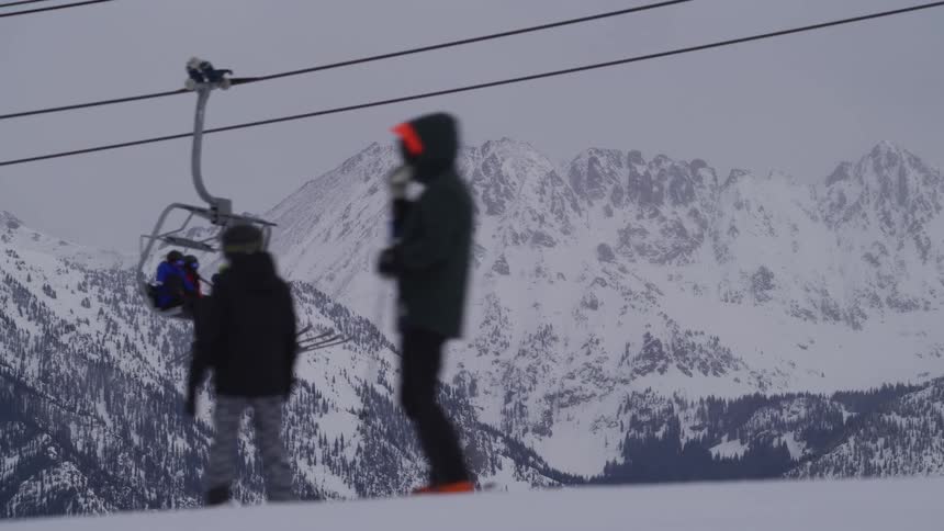 A ski lift carries people up the slope with a stunning view of snow-covered mountains in the background