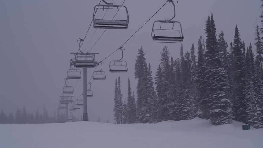 An empty ski lift operates in slow motion during a heavy blizzard on a desolate mountain