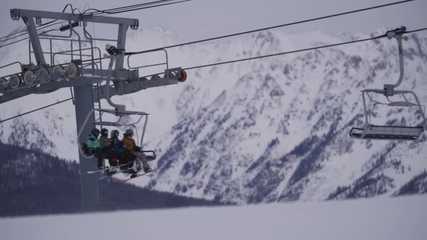 Slow motion view of a ski lift carrying people up the mountain with a dramatic snowy peak in the background