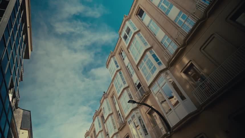 A seagull glides in slow motion through a city canyon between tall apartment buildings and against a blue sky