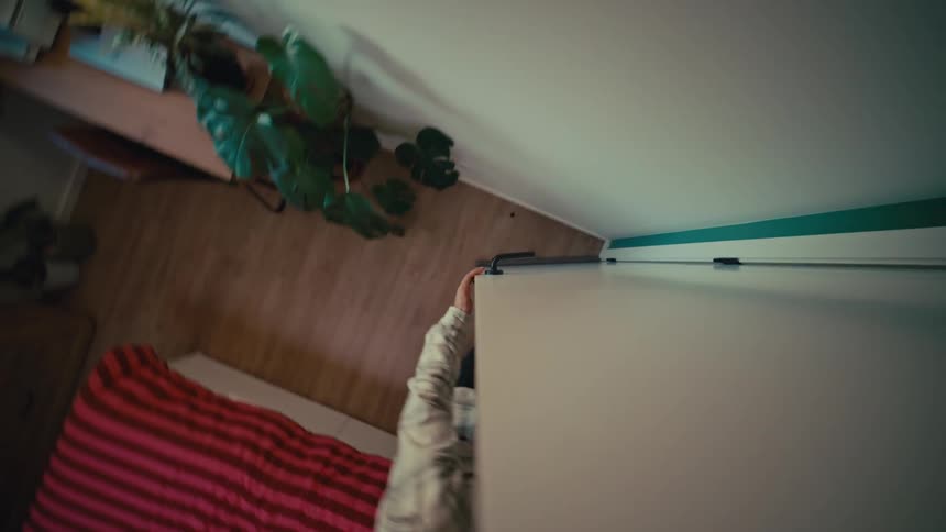 High-angle shot of a man walking through his bedroom and closing a white sliding closet door