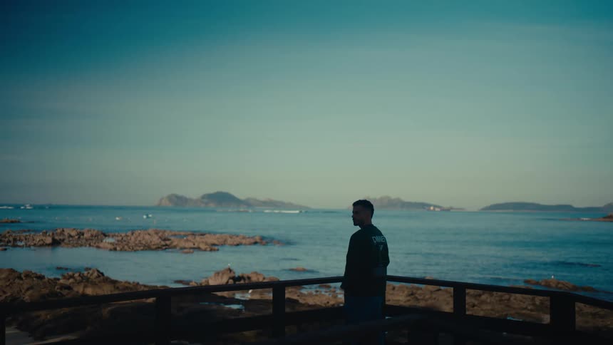 A man walks to a coastal viewpoint and peacefully gazes at the tranquil sea and distant islands