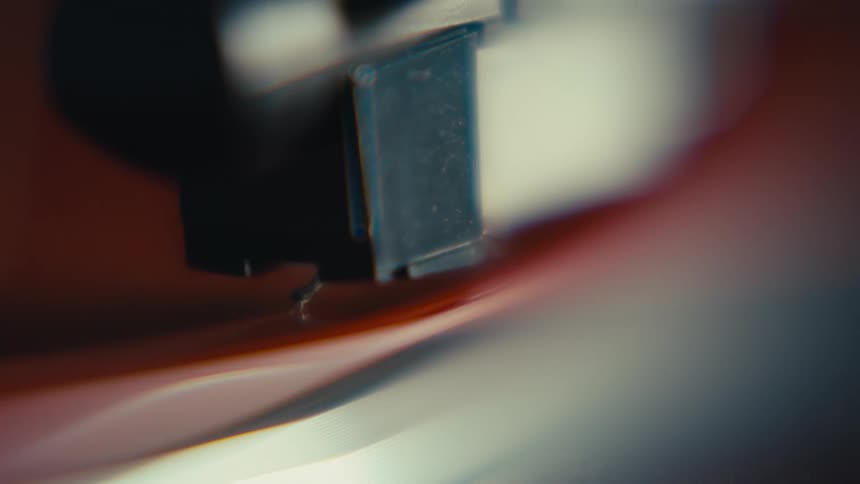 A dreamy, atmospheric macro shot shows a record player's stylus tracing the grooves of a spinning vinyl record