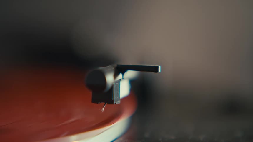 A shallow depth of field, close-up shot of a record player's stylus on a spinning red vinyl record