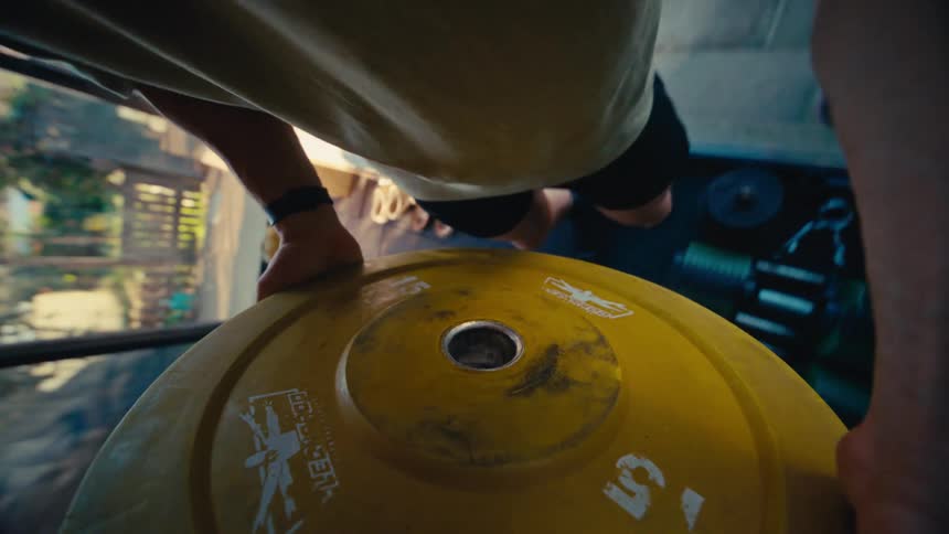 Unique spinning point of view from a weight plate as a man lifts a barbell in a home gym