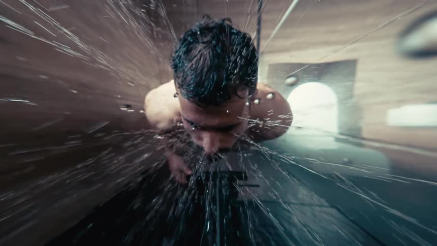 Dramatic overhead perspective of a man showering, with water droplets splashing in slow motion