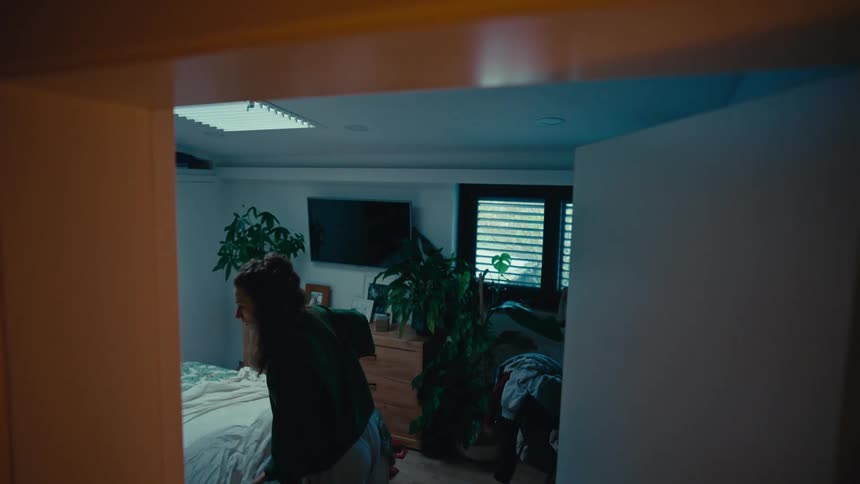 A woman makes her bed in slow motion in her cozy, plant-filled bedroom in the early morning