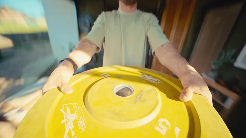 A unique first-person perspective shows a man doing intense push-ups on a yellow weight plate in a home gym