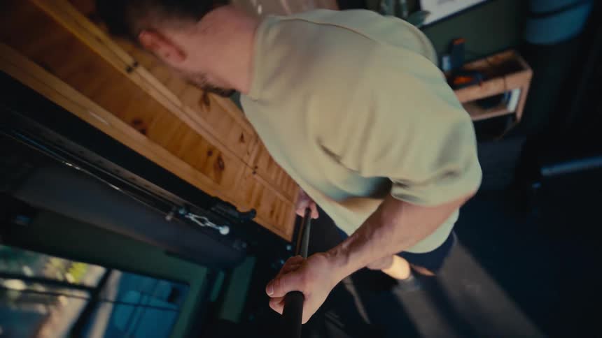 Dynamic high-angle, point-of-view shot of a man adjusting his camera on a selfie stick to film his workout in a home gym