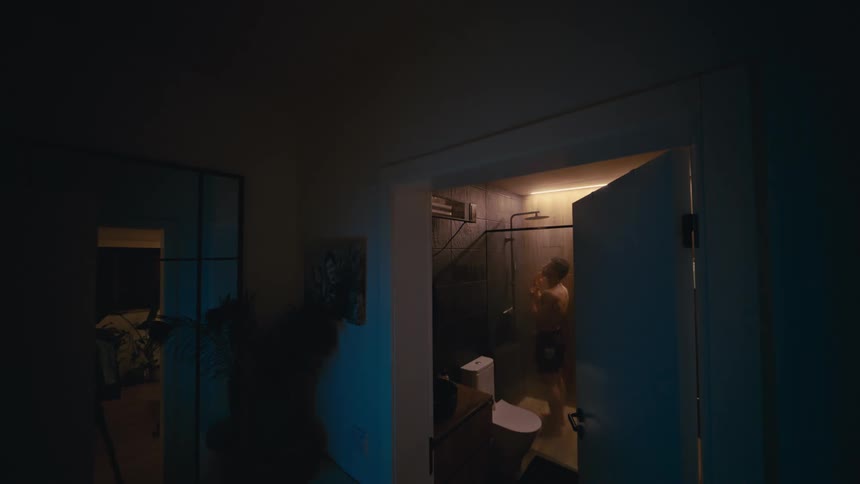 Atmospheric wide shot of a man taking a shower at night in his modern apartment bathroom