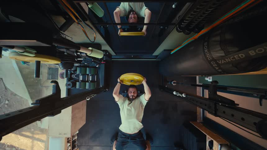 A focused man lifts a heavy weight plate while lying on a bench in a home gym, as seen from a high angle
