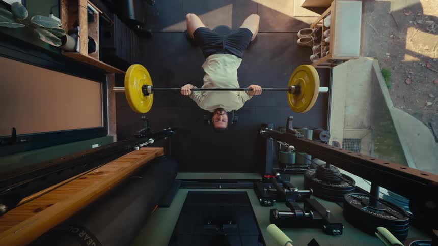 Top-down view of a man performing a bench press with a barbell in a modern home gym, creating a seamless loop